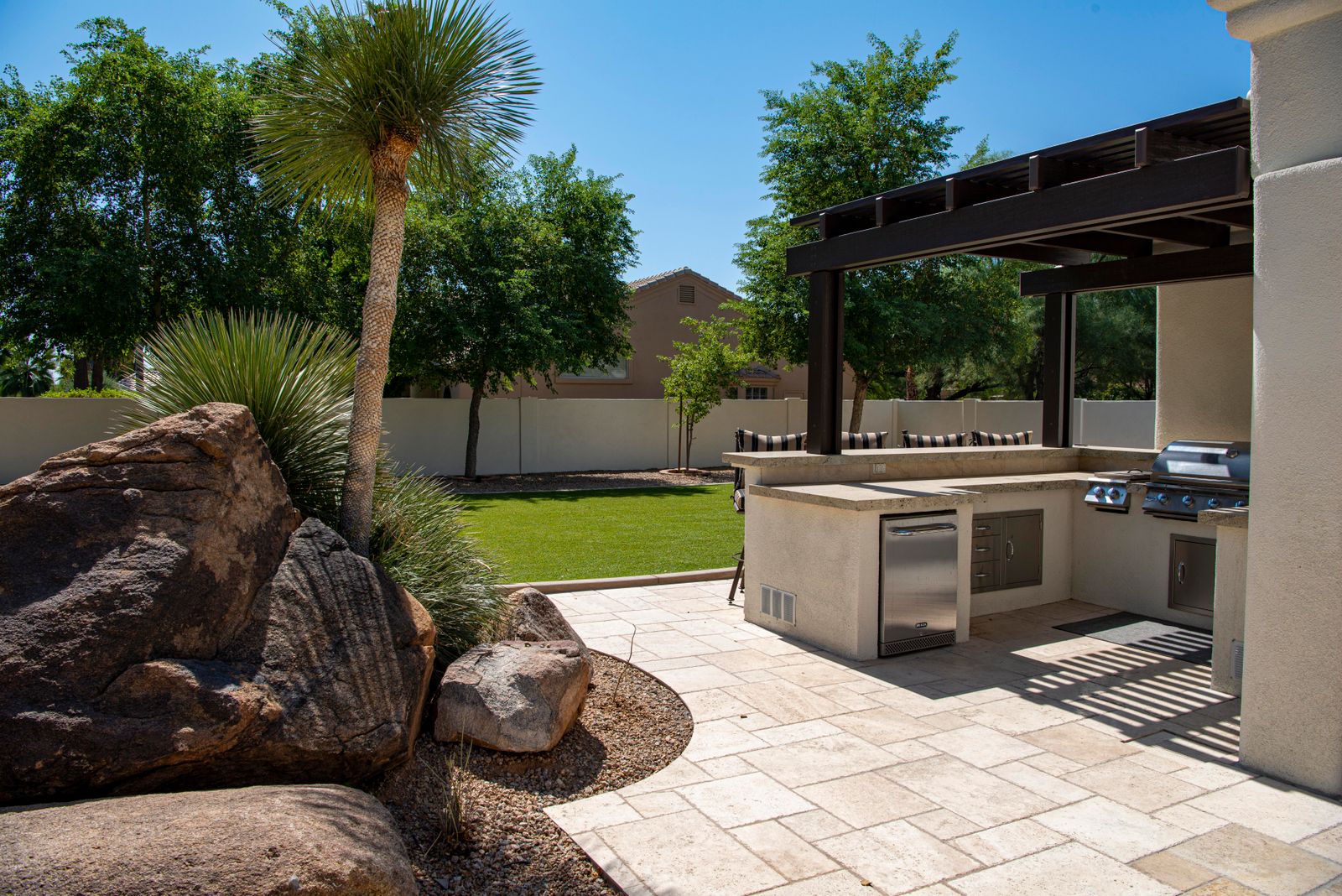 Outdoor kitchen with stone countertops on a sunny landscaped patio